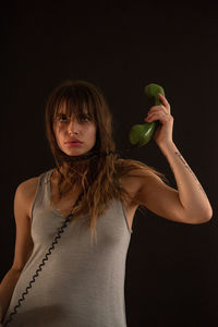 Portrait of young woman holding ice cream against black background