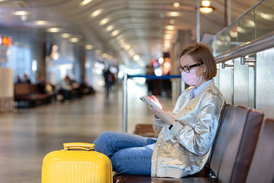 Woman using mobile phone while sitting by suitcaase at airport