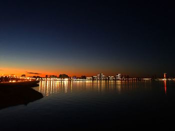 Illuminated city by sea against clear sky at night