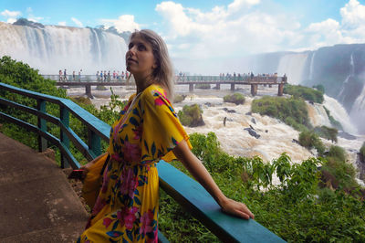 Woman looking away while standing against waterfall