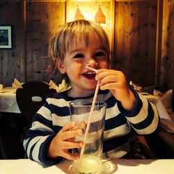 Smiling boy holding drinking glass with straw in restaurant