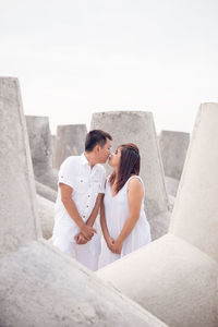 Couple kissing while standing amidst built structure against clear sky