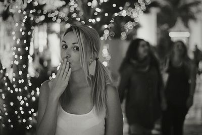 Portrait of young woman giving flying kiss by illuminated lights