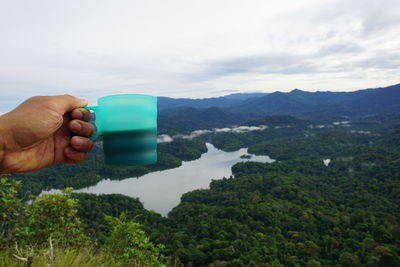 Midsection of person holding camera against mountains against sky