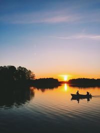 Silhouettes of two people in boat at sunset