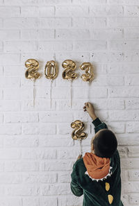 Little boy decorates the wall of the house with golden numbers 2023. change numbers