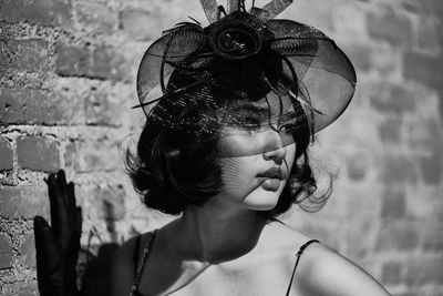 Girl wearing hat looking away while standing against brick wall