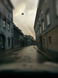 Wet road amidst buildings against sky