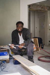 Portrait of cheerful carpenter with measuring instrument and plank in apartment