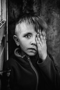 Portrait of boy hiding on eye by hand against wall