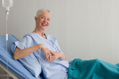 Portrait of smiling senior woman sitting on bed in hospital