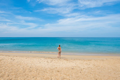 Rear view of woman standing on beach against sky