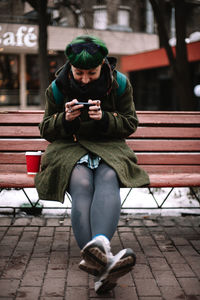 Full length of man using mobile phone while sitting on seat