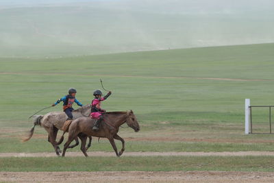 Horses riding horse on field