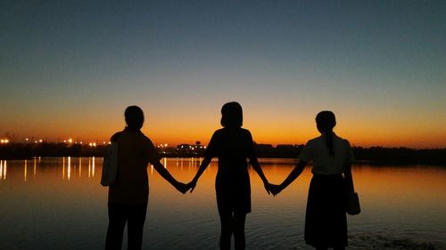 Silhouette people standing by sea against sky during sunset