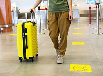 Woman traveler in casual carrying yellow suitcase at check-in desk at airport terminal tourism 