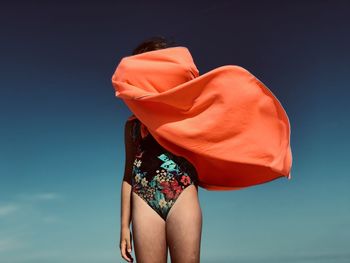 Low angle view of girl wearing swimwear standing against blue sky