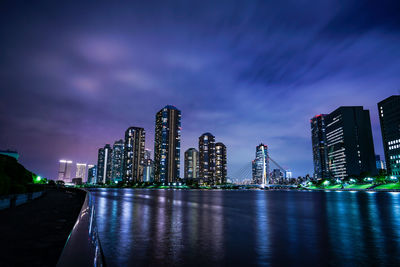 Illuminated modern buildings in city against sky at night