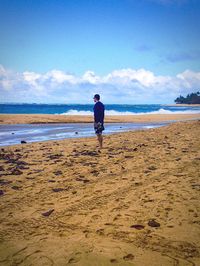 Rear view of man standing on beach against sky