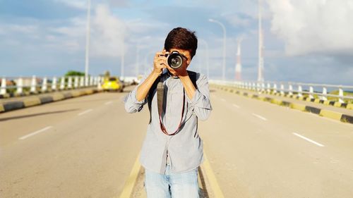 Woman photographing with umbrella standing on road against sky