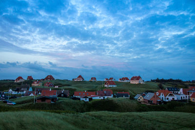 Houses on field by town against sky