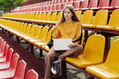 A young girl is doing her homework using a laptop in the stands of the stadium. 