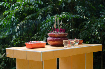 Incense with drinking glasses on table against trees