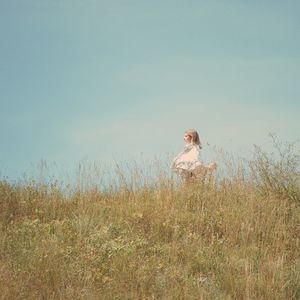 Young woman standing on field against sky