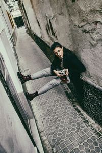 High angle portrait of young woman photographing while smoking cigarette on wall 