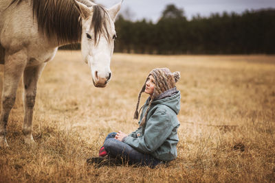 Young girl sitting in field in front of white horse
