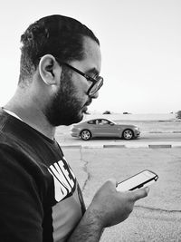 Close-up of young man using smart phone against sky