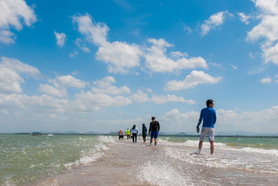 Rear view of people on beach against cloudy sky