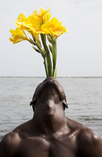Close-up of shirtless man with flowers in mouth against sea