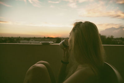 Rear view of woman holding umbrella against sky during sunset