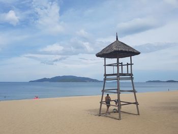 Shirtless man standing by lifeguard hut at beach