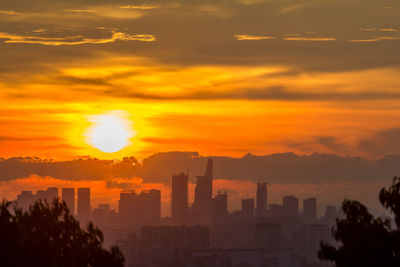 Silhouette of city against cloudy sky during sunset