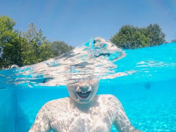 Water surface shot of shirtless boy swimming in pool during sunny day