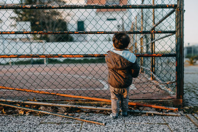 Rear view child looking through chailink fence