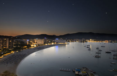 Illuminated city by sea against sky at night