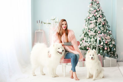 Portrait of smiling woman with dogs sitting by christmas tree