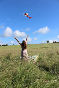 Rear view of woman with arms raised standing on grassy field against sky