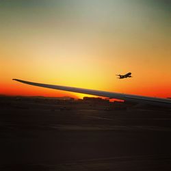 Silhouette airplane flying in sky at sunset