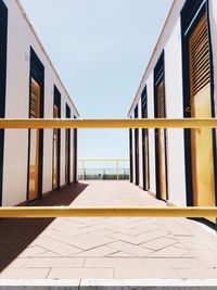 Empty footpath amidst buildings against sky on sunny day