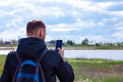 Bearded man in black raincoat on blue sea landscape with smartphone in hands talking calling friends