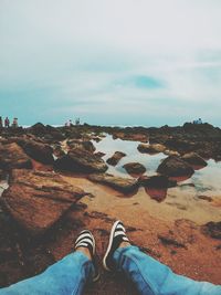 Low section of person on rock by sea against sky