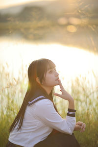 Side view of young woman standing against trees