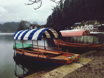 Boats moored on river by trees against sky