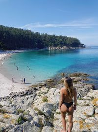 Rear view of woman standing at blue sea beach against sky