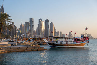 Boats in sea by buildings against clear sky