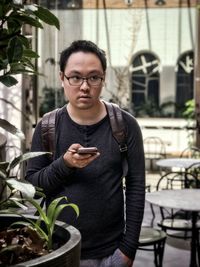 Portrait of young man standing against potted plants